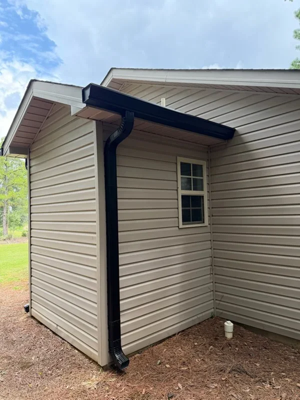 Black downspout and gutter system on tan vinyl siding with proper drainage routing