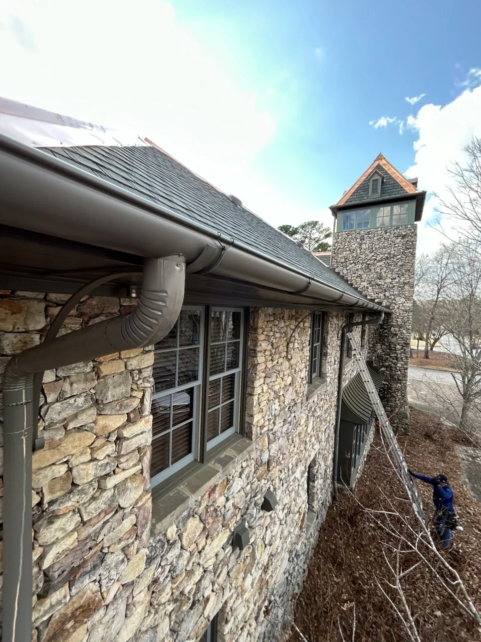 Metal gutter and downspout installation on stone cottage exterior