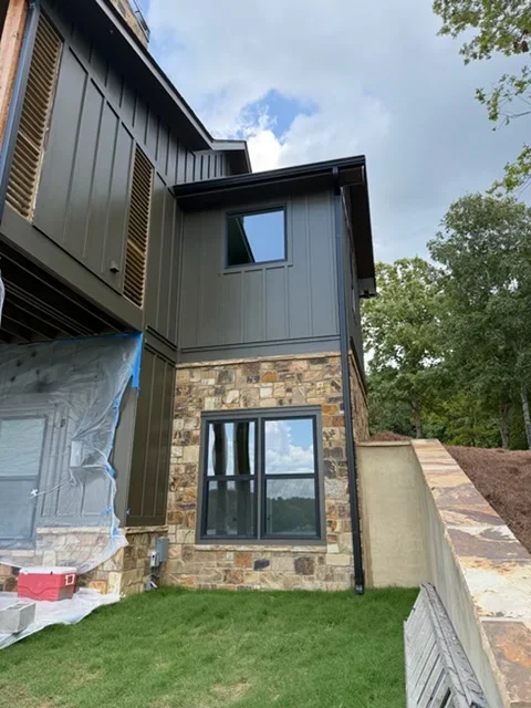 Two-story addition with charcoal metal siding, stone veneer base, black-framed windows, and integrated gutters