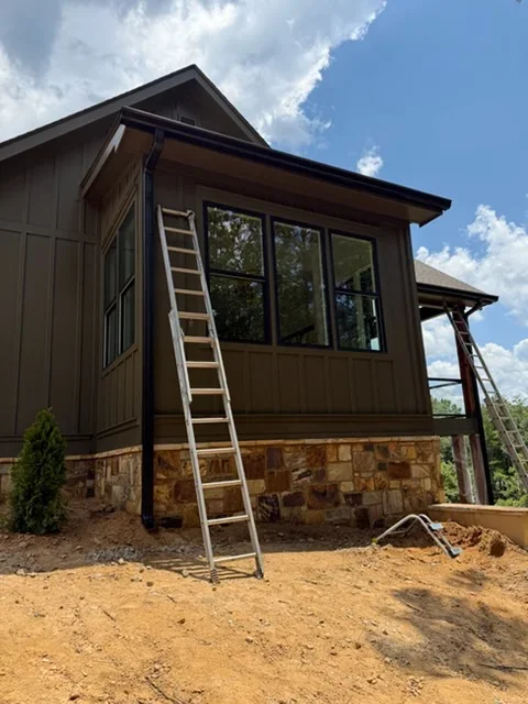 Dark metal siding home with stone foundation, large windows, and integrated gutter system