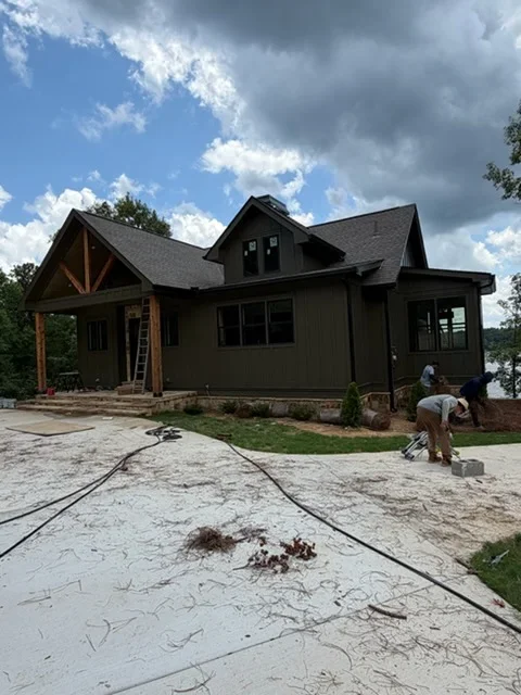 Dark siding farmhouse with installed gutters, timber accents, and gable roof during construction