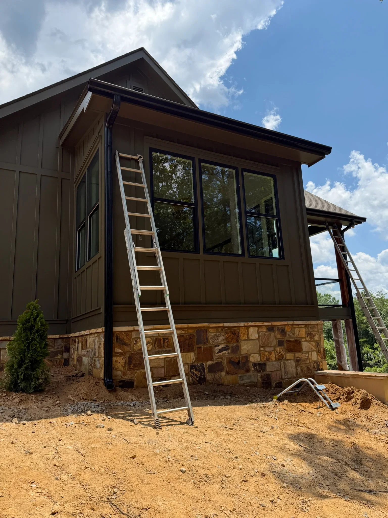 Dark metal gutters and downspouts installed on modern home with black trim and stone foundation